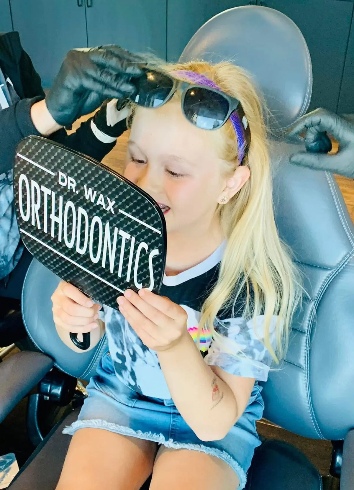 Child smiling at reflection in Dr. Wax Orthodontics mirror, feeling confident after a caring visit.