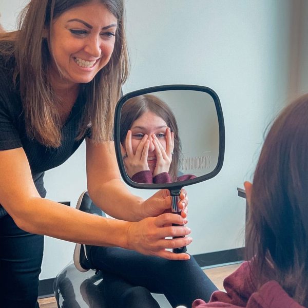 Orthodontist shares a joyful moment with a smiling patient seeing her reflection.