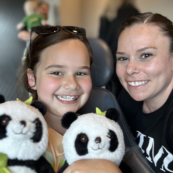 Child with braces and orthodontist sharing a joyful moment with stuffed pandas.