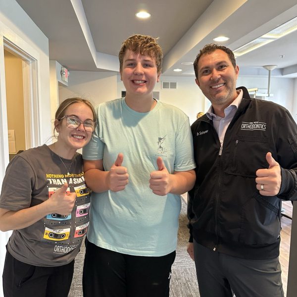 A happy teen shares a thumbs-up moment with Dr. Wax and a caring team member, spreading smiles together.