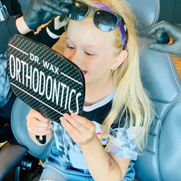 Child smiling at reflection in Dr. Wax Orthodontics mirror, feeling confident after a caring visit.