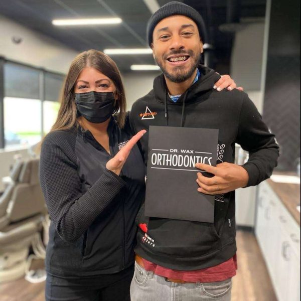Smiling braces patient holding Dr Wax Orthodontics sign with staff member celebrating new braces in Smyrna TN orthodontic office